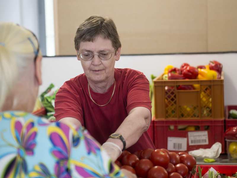 Eine Mitarbeiterin der Tafel gibt Tomaten und Paprika aus.
