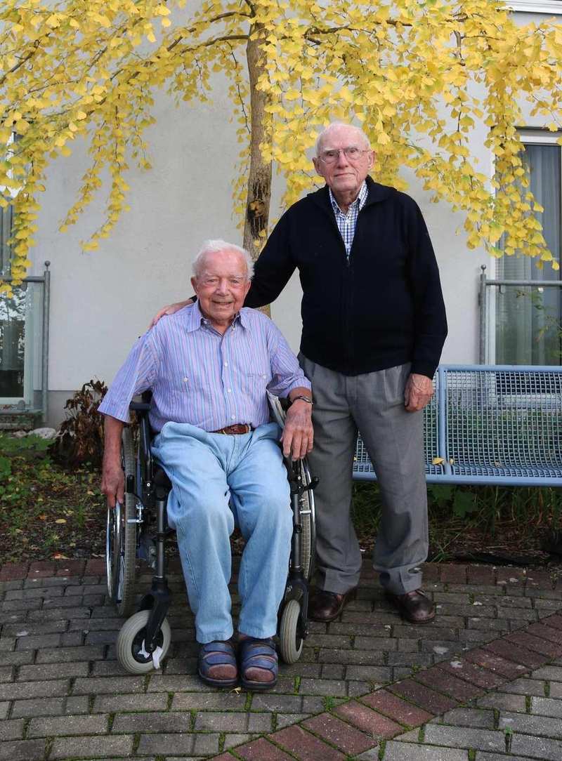 Zwei ältere Männer sind im Außenbereich der Diakonie Sophienstraße. Ein Mann sitzt im Rollstuhl, der andere steht neben ihm. Hinter den beiden befindet sich eine Bank und eine große Birke.