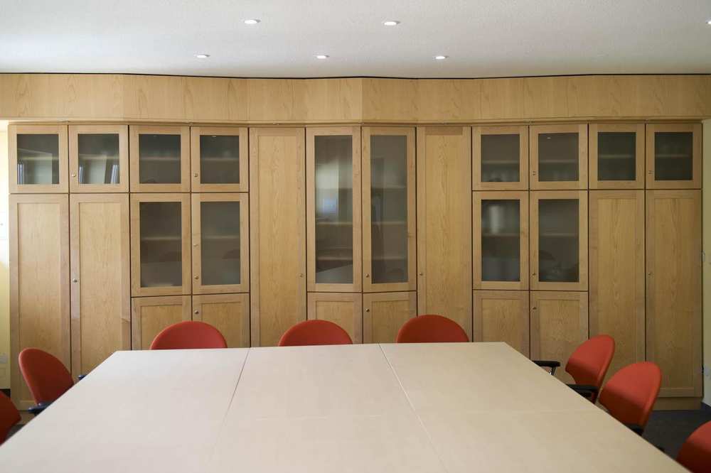 Eine komplette Inneneinrichtung, bestehend aus fünf miteinander verbundenen Wandschränken aus hellem Holz. Die Schranktüren sind zum Teil verglast.
