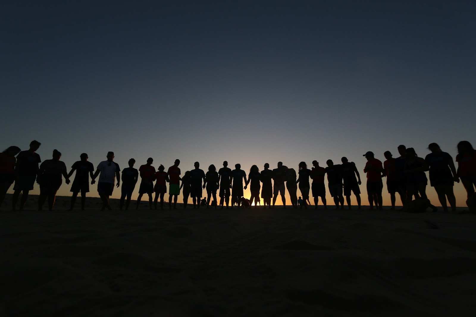 An einem Horizont mit aufgehender Sonne steht eine Menschenkette.