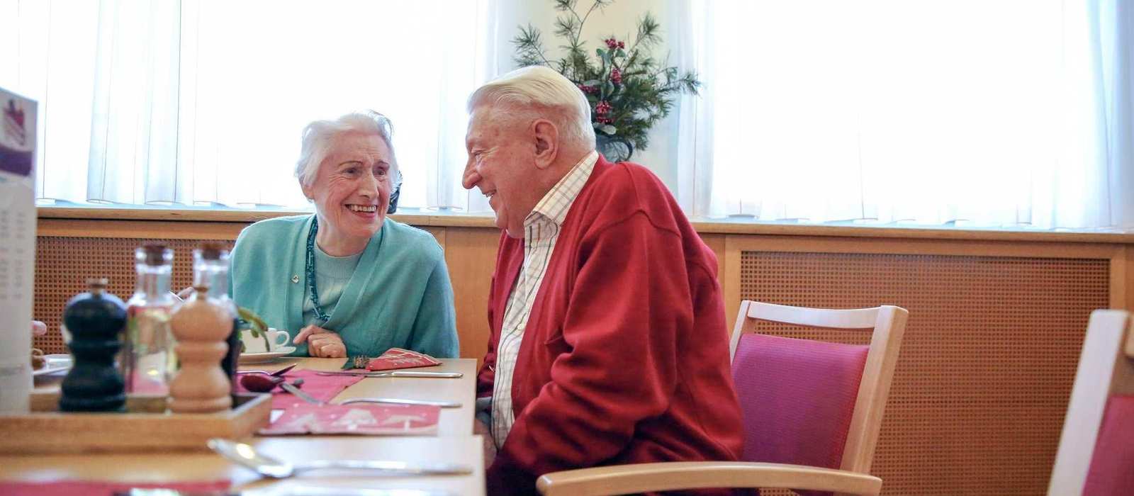 Zwei ältere Personen sitzen an einem Tisch und unterhalten sich.