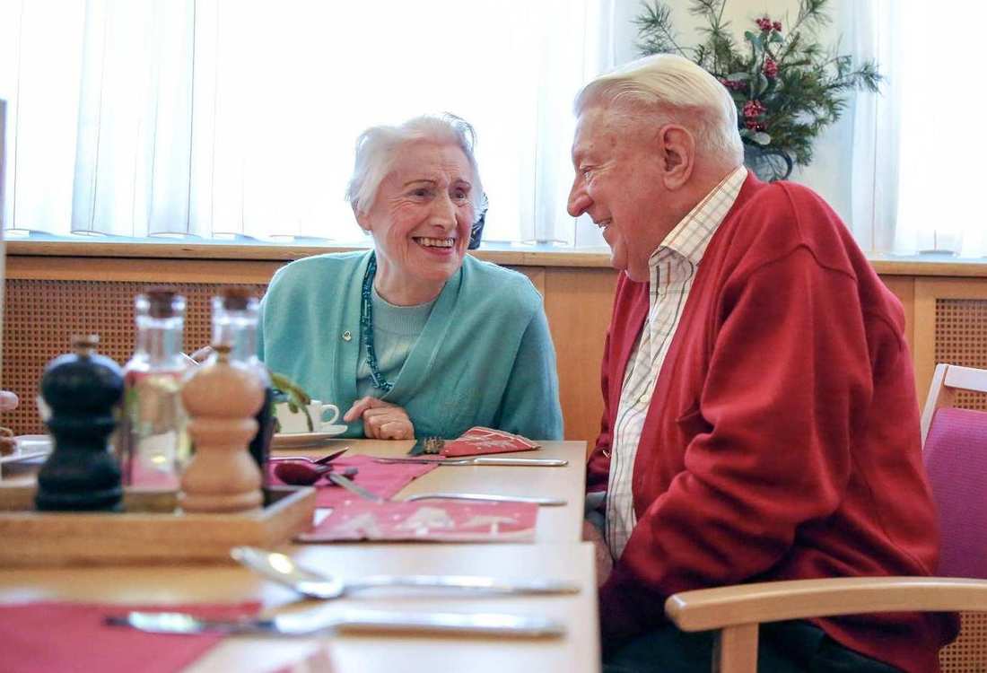 Zwei ältere Personen sitzen an einem Tisch und unterhalten sich.