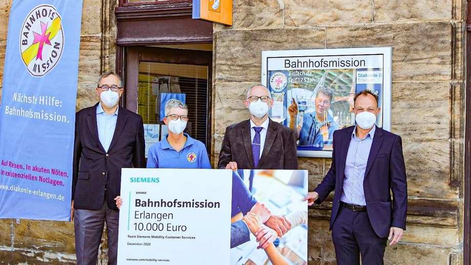 Siemensmitarbeitende übergeben den symbolischen Spendenscheck an die Bahnhofsmission Erlangen.