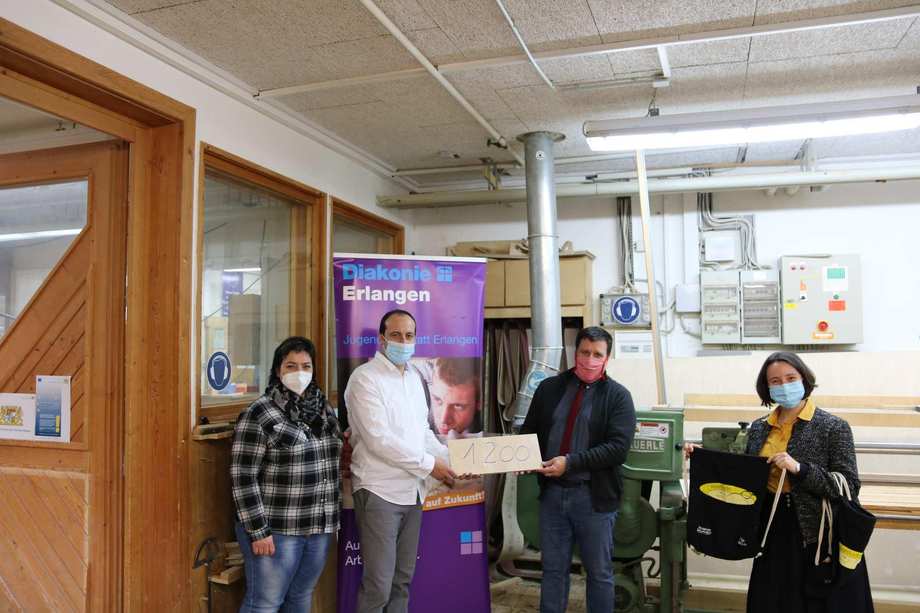Vier Personen stehen in einem Werkstattraum und halten ein Holzschild mit der Zahl 1200 Euro.