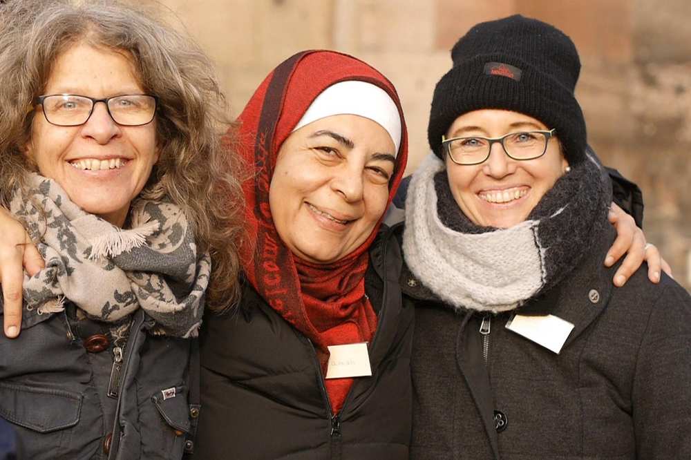 Drei Frauen lachen Arm in Arm in die Kamera.