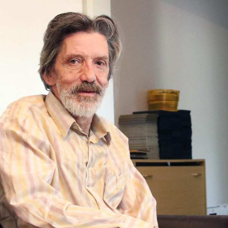 Ein älterer Mann mit Bart und längeren grauen Haaren sitzt in einem Sessel.